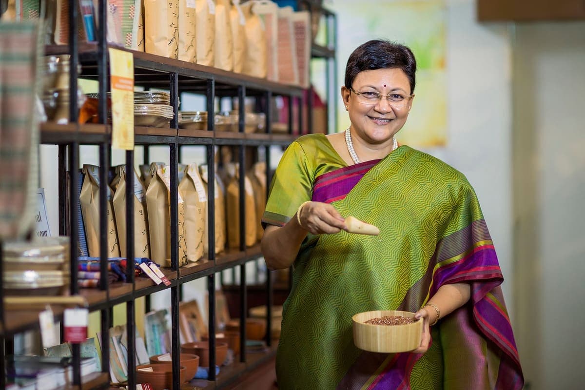 A founder in a sari weighing product behind the counter of her shop.
